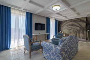 A living room with a TV, blue and white patterned sofa, wooden chairs, and a stone wall mural.