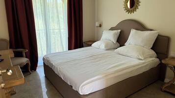 Una cama grande con sábanas blancas, una mesita de noche de madera, una silla y una ventana con cortinas.