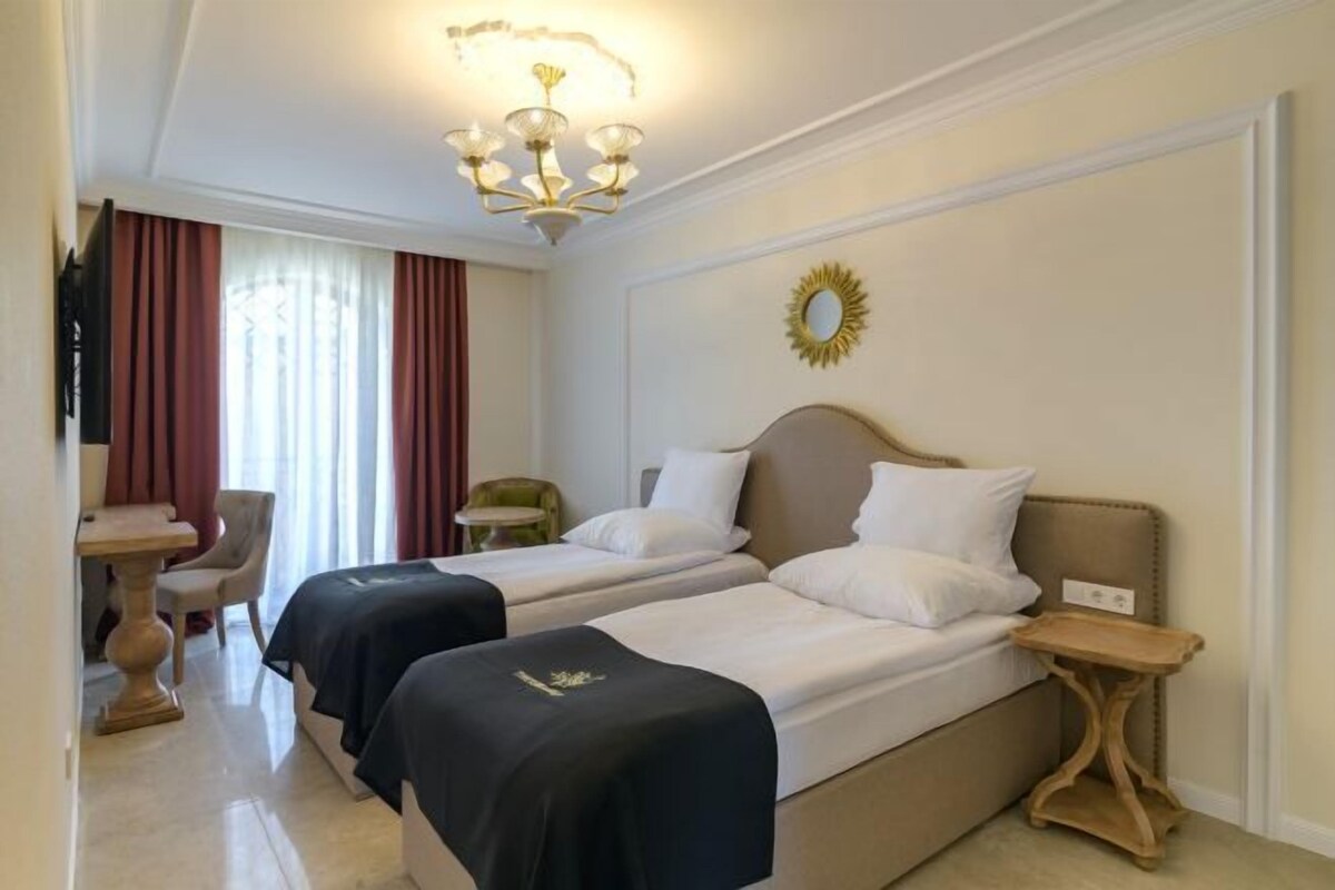 A hotel room with two beds, a chandelier, a round mirror, and a small table.