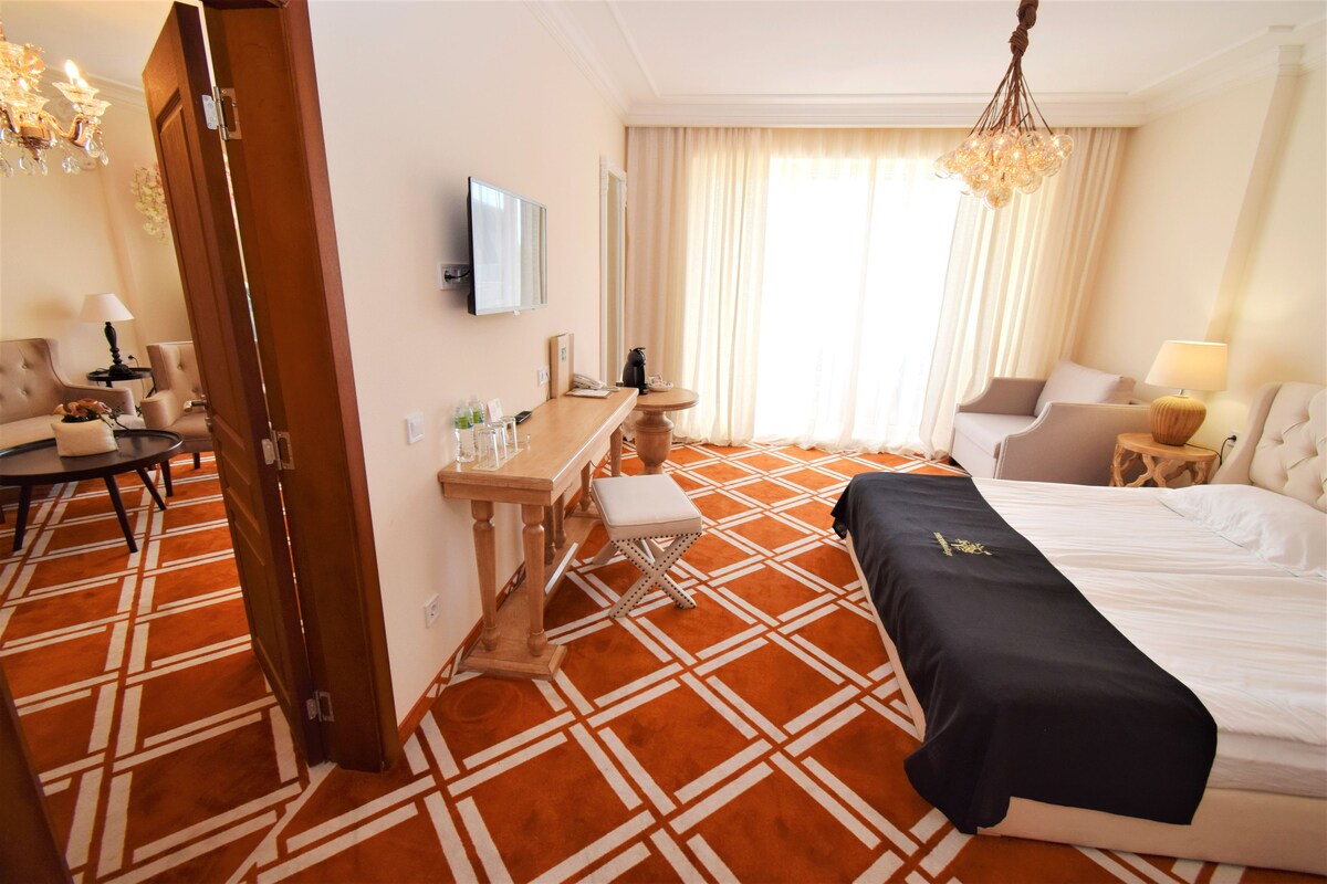A hotel room with a large bed, a desk with a chair, a television, and a chandelier.