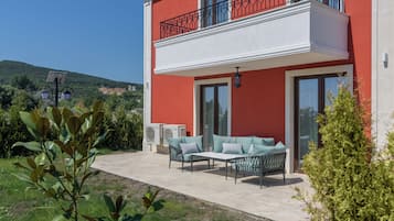 A two-story building with a red exterior, a balcony with black railings, and a patio area with outdoor furniture.