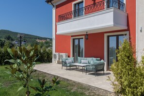 Un edificio de dos plantas con fachada roja, un balcón con barandillas negras y un patio con muebles de exterior.