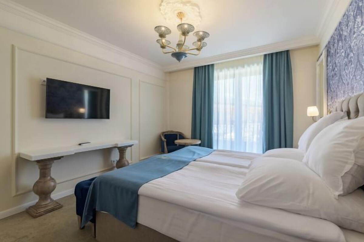 A hotel room with a large bed, a flat-screen TV mounted on the wall, a small table, and a chair.
