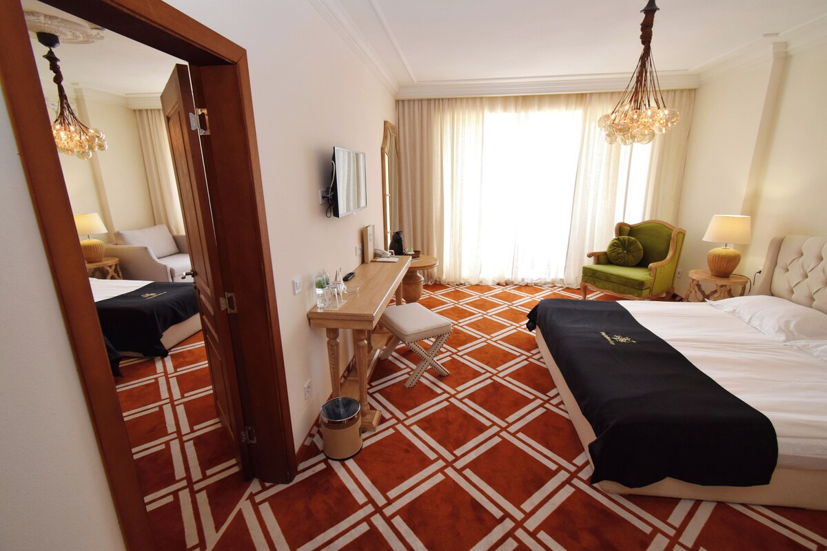 A hotel room with a bed, a desk, a chair, a mirror, and a window with curtains.
