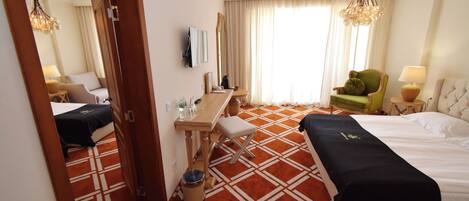 A hotel room with a bed, a desk, a chair, a mirror, and a window with curtains.