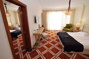 A hotel room with a bed, a desk, a chair, a mirror, and a window with curtains. - Eco Therma Village Spa & Sport (Balchik)