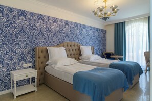 A room with two beds, a nightstand, a small table, and a chandelier.