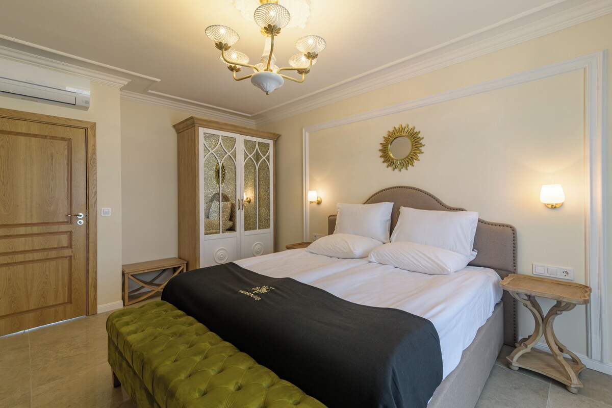 A bedroom with a large bed, a chandelier, a wooden wardrobe, and a mirror on the wall.