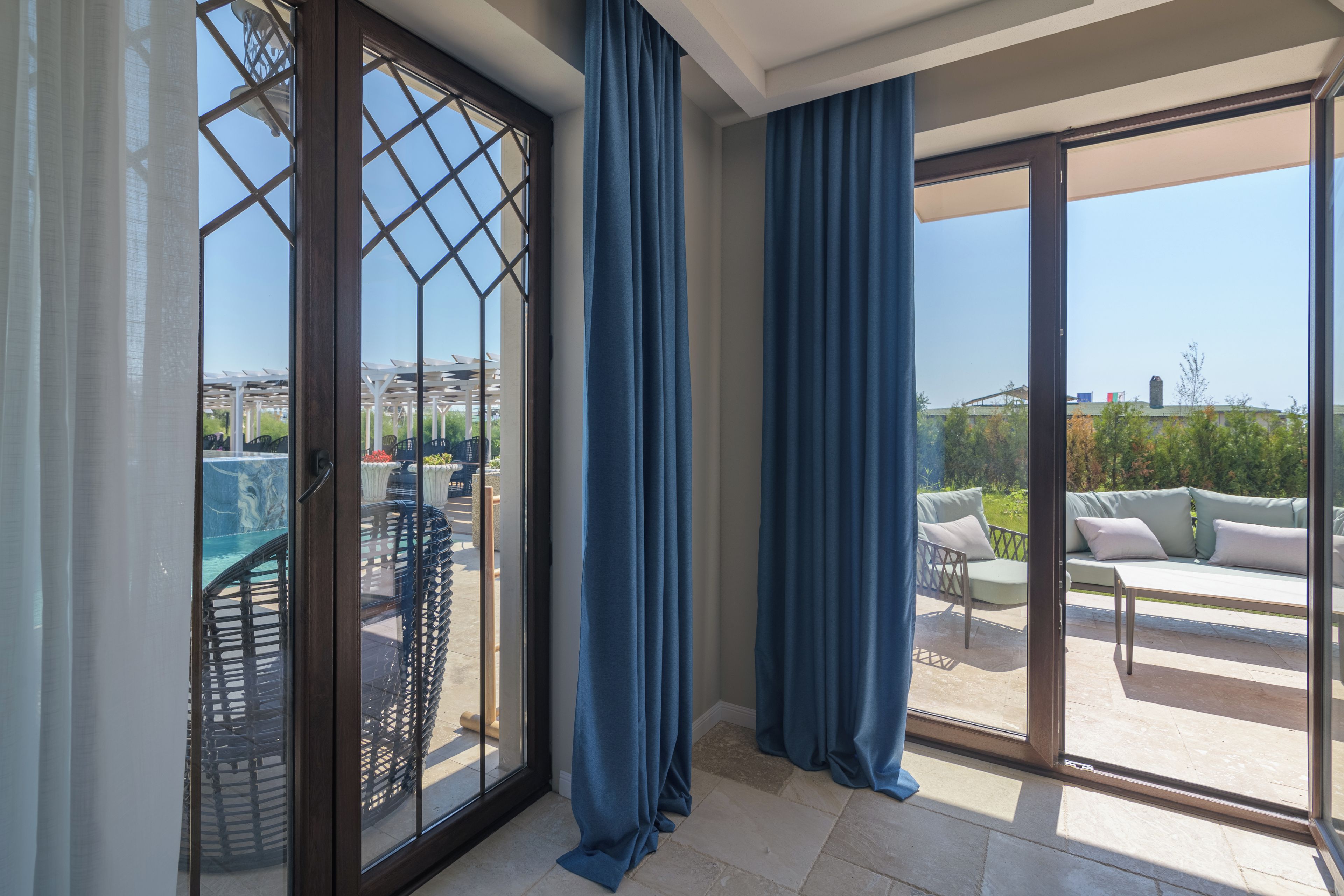 Une pièce dotée d’une porte-fenêtre coulissante donnant sur une terrasse extérieure avec une piscine et du mobilier.