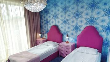 Quarto de hotel com duas camas, um candelabro, parede com padrão azul e uma janela com cortinas.