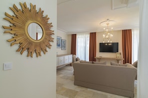 A living room with a beige sofa, a sunburst mirror, a flat-screen TV, and a chandelier. - Eco Therma Village Spa & Sport (Balchik)
