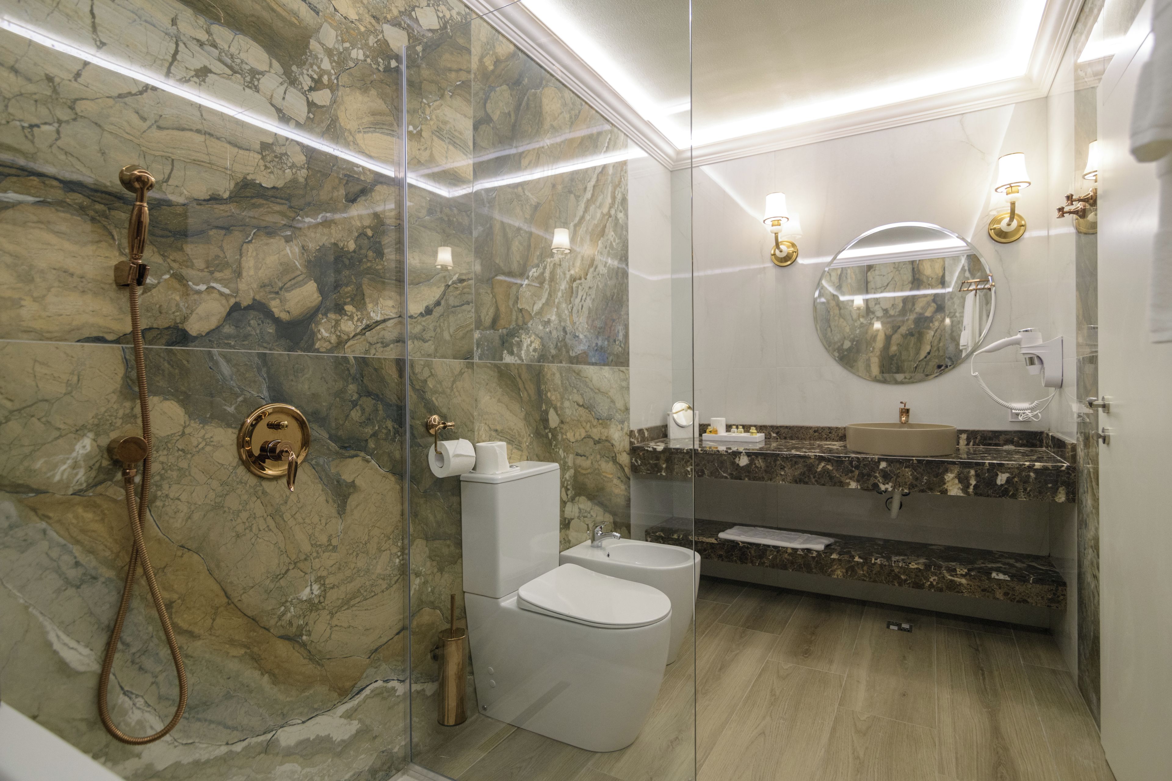 Ein modernes Badezimmer mit Marmorwand, einer Glaskabine für die Dusche, einer Toilette, einem Bidet und einem Waschtisch.