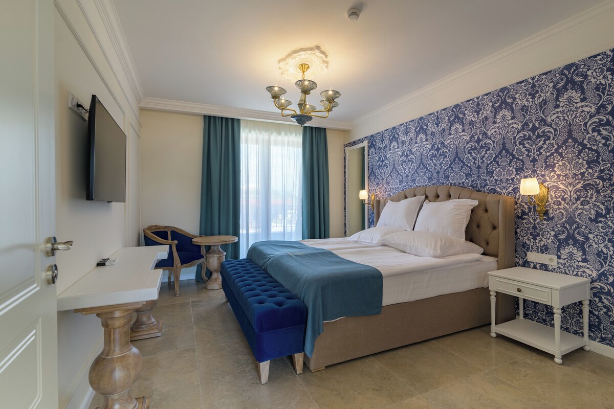 A bedroom with a bed, a bedside table, a chair, a bench, a TV, and a patterned wall.