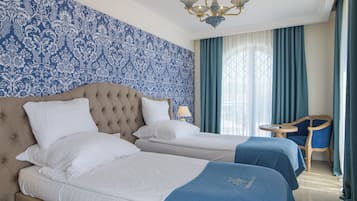 A hotel room with two beds, a chandelier, a table, and a chair.