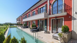 A two-story building with a swimming pool, outdoor seating, and a red facade. - Eco Therma Village Spa & Sport (Balchik)