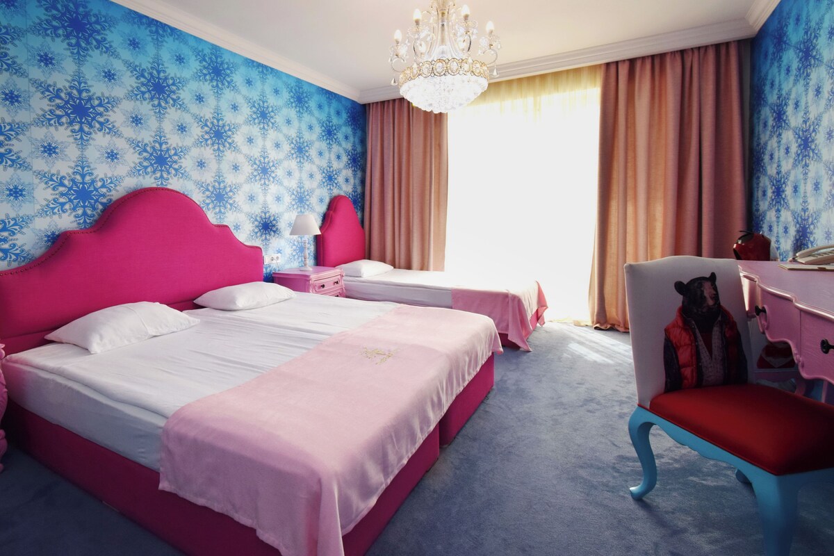 A hotel room with two beds, a chandelier, a desk, and a chair.
