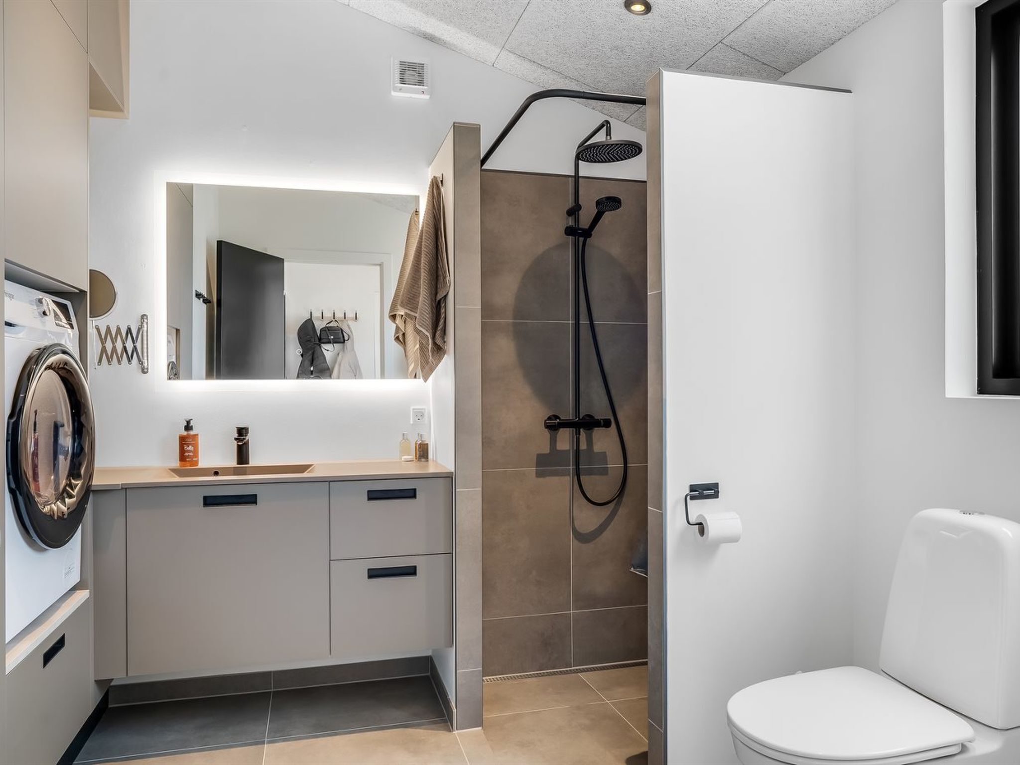 Moderni kylpyhuone, jossa on sisäänrakennettu pesukone, käsisuihkulla varustettu suihku ja wc.