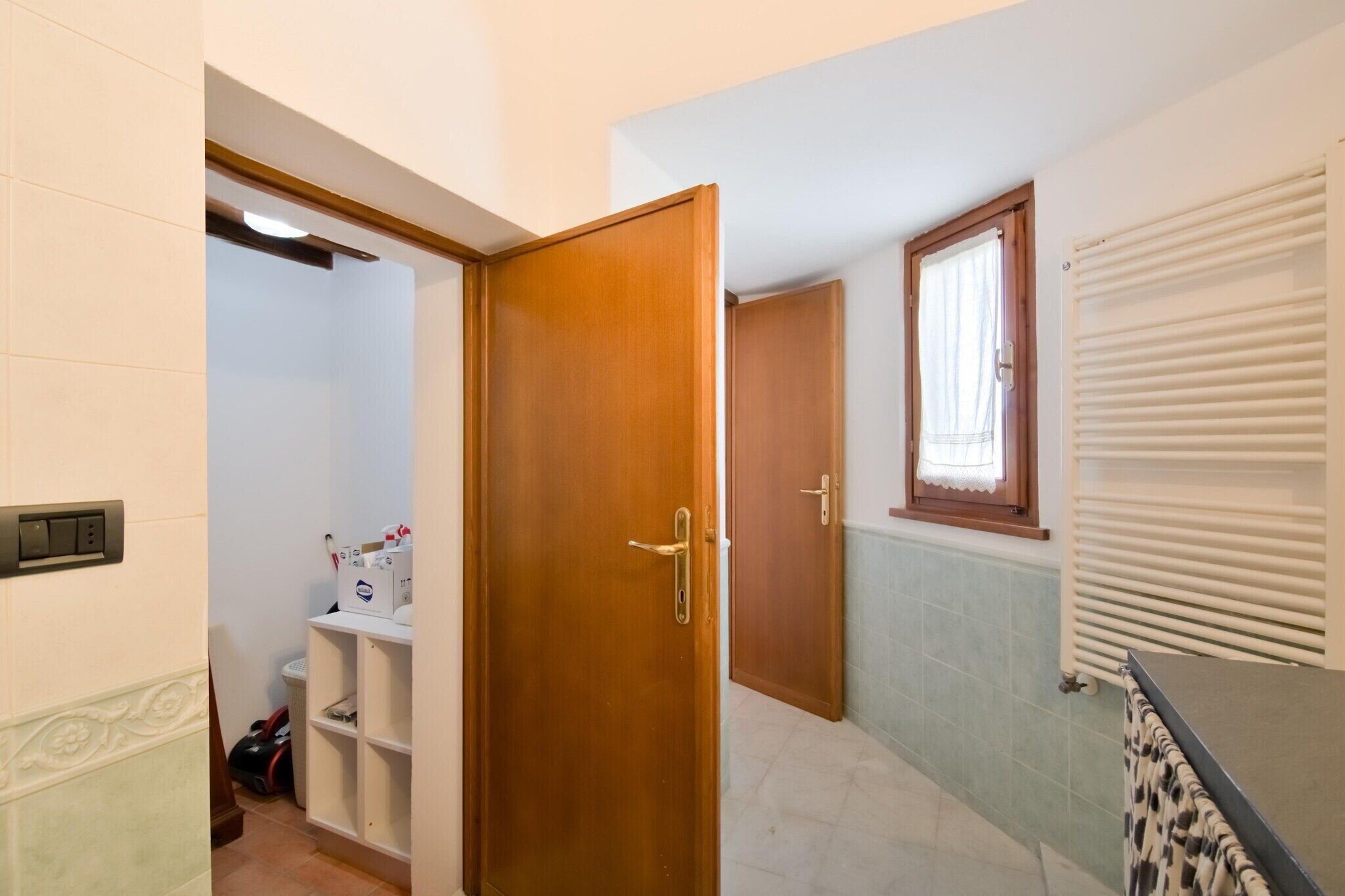 Ein Badezimmer mit Holztür, Heizkörper und einem fenster mit Vorhang.