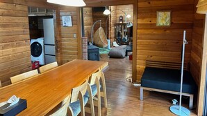 A wooden cabin interior with a dining area, a bed, and a washing machine. - SHODOSHIMA PRIVATE CAMP SITE (Shodoshima)