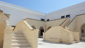 A courtyard with a central staircase, stone walls, and arched doorways. - Mare Nostrum Hotel (Fasano)