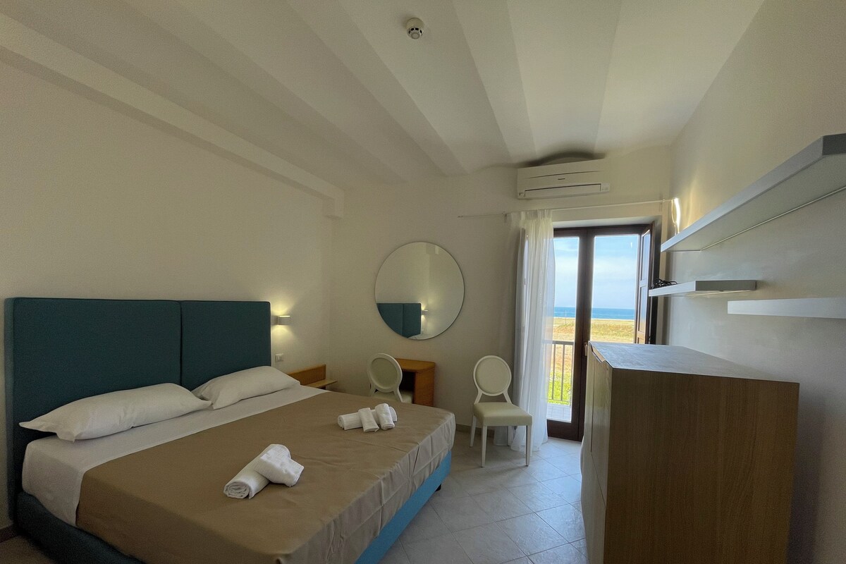 Ein Hotelzimmer mit Bett, Schreibtisch, Stuhl, Spiegel und Blick auf den Strand.