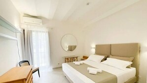 A hotel room with a bed, a desk, a chair, a round mirror, and an air conditioning unit. - Mare Nostrum Hotel (Fasano)