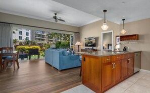 A modern hotel room with a living area, kitchenette, and a balcony with a view of the hotel buildings and greenery.