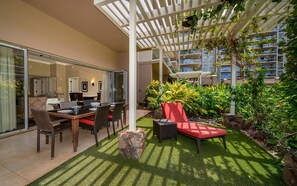 A modern outdoor seating area with a dining table and chairs, surrounded by lush greenery and a pergola structure.