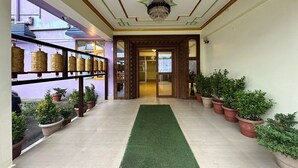 A hallway with a green carpet, potted plants, and shelves with golden objects. - Hotel Tashi Ga-Tsel (Tawang)