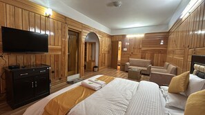 A hotel room with wooden paneling, a flat-screen TV, a bed with white and gold bedding, a sofa, and a small table. - Hotel Tashi Ga-Tsel (Tawang)