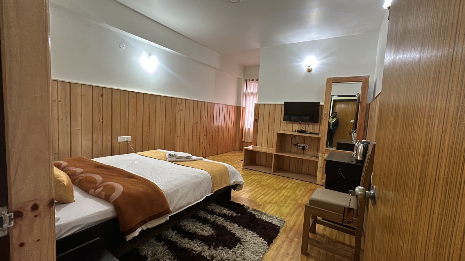 Un dormitorio con dos camas, televisión, paneles de madera, un espejo y un escritorio pequeño.