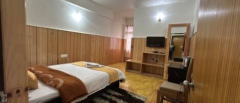 Un dormitorio con dos camas, televisión, paneles de madera, un espejo y un escritorio pequeño.