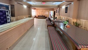 A spacious, well-lit room with wooden paneling, a long counter, and several benches. - Hotel Tashi Ga-Tsel (Tawang)