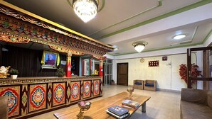 A reception area with a traditional decorative wall, a reception desk, a chandelier, and a seating area with a table and cushions. - Hotel Tashi Ga-Tsel (Tawang)