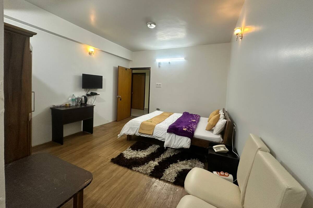 A compact hotel room with a bed, a desk, a chair, a television, and a door.