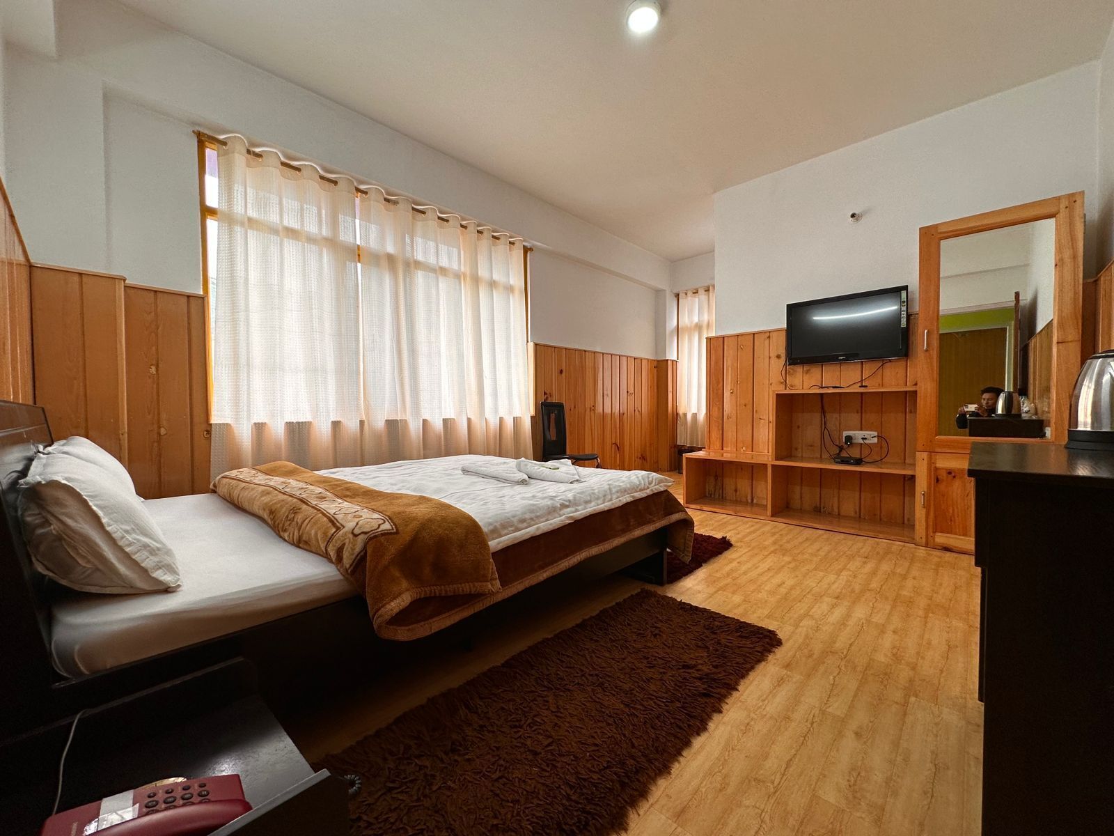Un dormitorio con cama, armario de madera, televisor y espejo.
