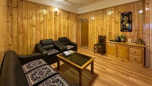 A room with wooden paneling, a chandelier, a sofa with patterned cushions, a coffee table, and a cabinet with decorative items. - Hotel Tashi Ga-Tsel (Tawang)