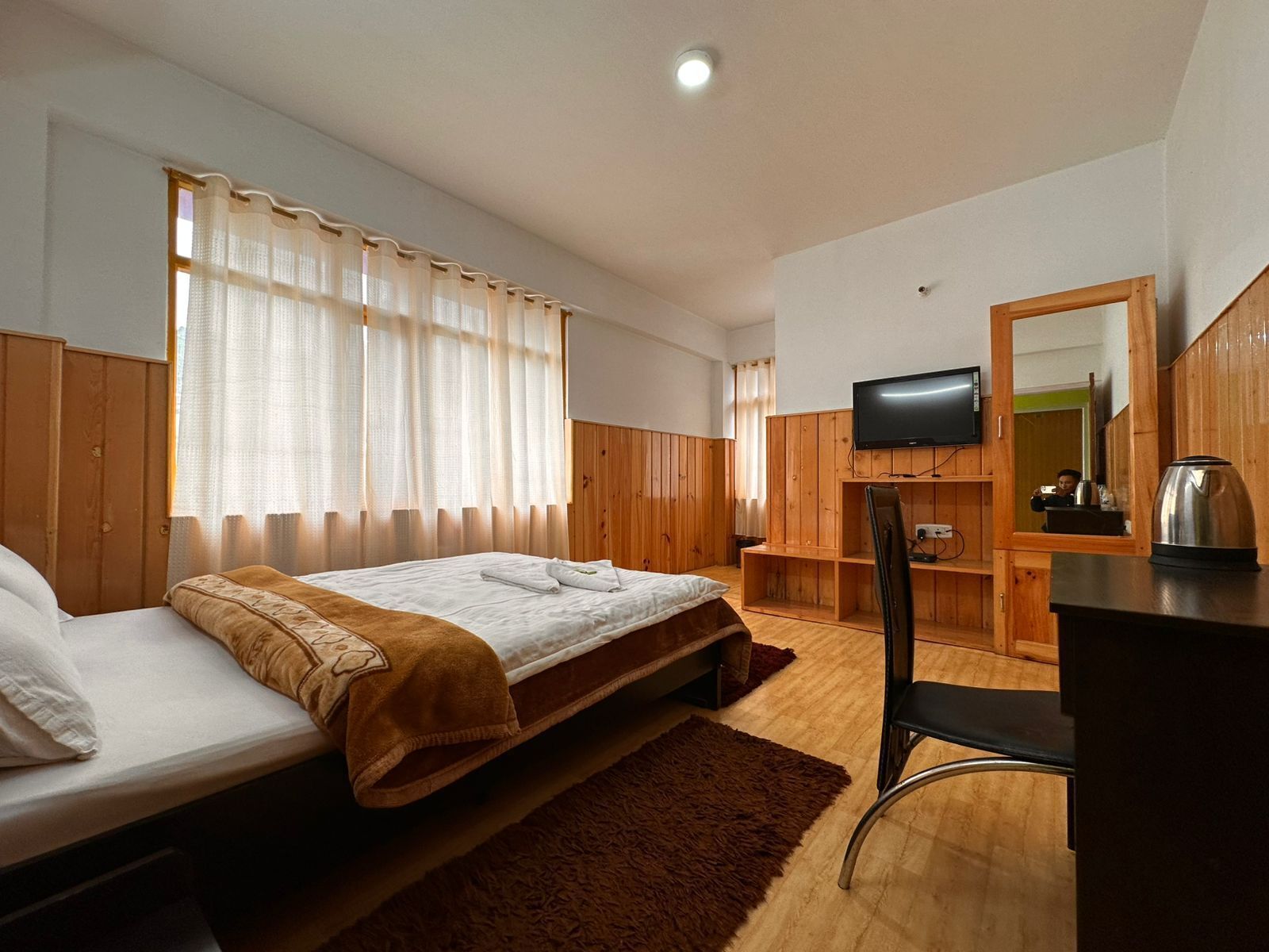 A bedroom with a bed, a desk, a chair, a television, and a mirror.