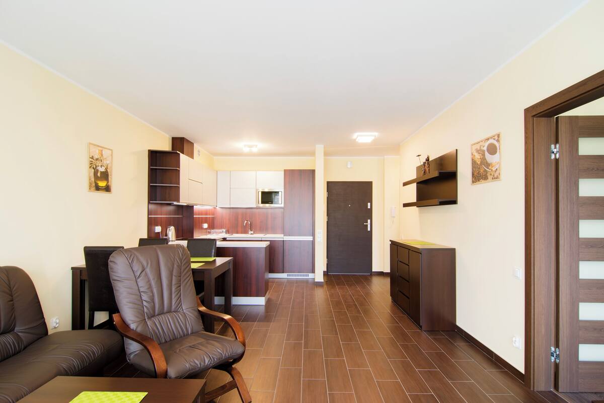 A modern living room with a sofa, a dining table, and a kitchen area in the background.