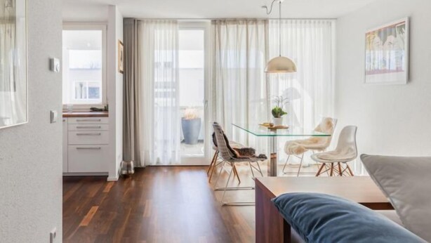 Un salon moderne avec une table à manger en verre, un canapé et une vue dégagée sur l’extérieur grâce à une grande fenêtre.