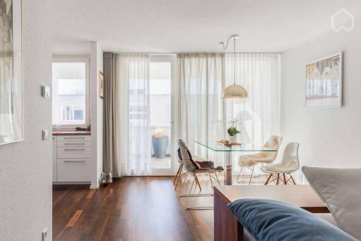 Un salon moderne avec une table à manger en verre, un canapé et une vue dégagée sur l’extérieur grâce à une grande fenêtre.