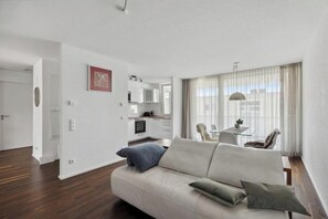A modern living room with a sofa, a dining area with a table and chairs, and a kitchen in the background. - EXQUIS 2BR Luxury Apt. ROLF BENZ Parking Centre Kitchen Pick-up Service Airport (Boblingen)