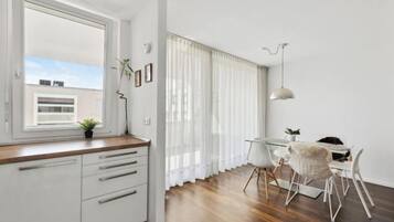 Eine moderne Küche mit Fenster, weißen Schränken und einem Essbereich mit Tisch und Stühlen.