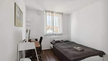 Eine kleine, einfache Unterkunft mit Bett, Schreibtisch, Stuhl und einem blickdichten Fenster.