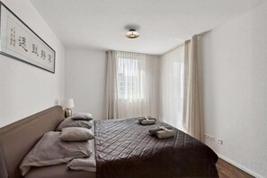 Ein Hotelzimmer mit Bett, Nachttisch, Lampe und einem Fenster mit Vorhängen.