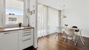 Une cuisine moderne avec des meubles blancs, un plan de travail en bois et une fenêtre donnant sur des immeubles.