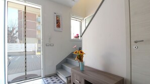 A modern interior with a sliding glass door leading to a balcony, a wooden console table with a vase of flowers, and a calendar on the wall. - Stunning  villa for 6 people with A/C, WIFI, TV, terrace and pets allowed (Lido Degli Estensi)