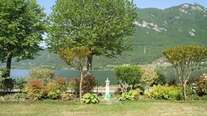 A serene lakeside park with lush greenery, a white fountain, and a backdrop of mountains. - Villa by Lake Idro with Mountain Views (Idro (bs))