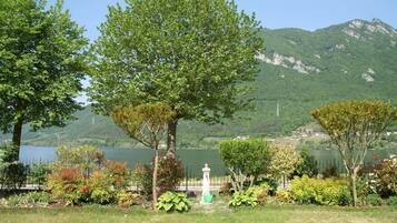 Un parque tranquilo junto al lago, con abundante vegetación, una fuente blanca y montañas al fondo.