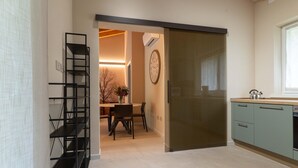 A modern kitchen with a sliding door, a dining area with a table and chairs, and a black metal shelving unit. - Villa by Lake Idro with Mountain Views (Idro (bs))